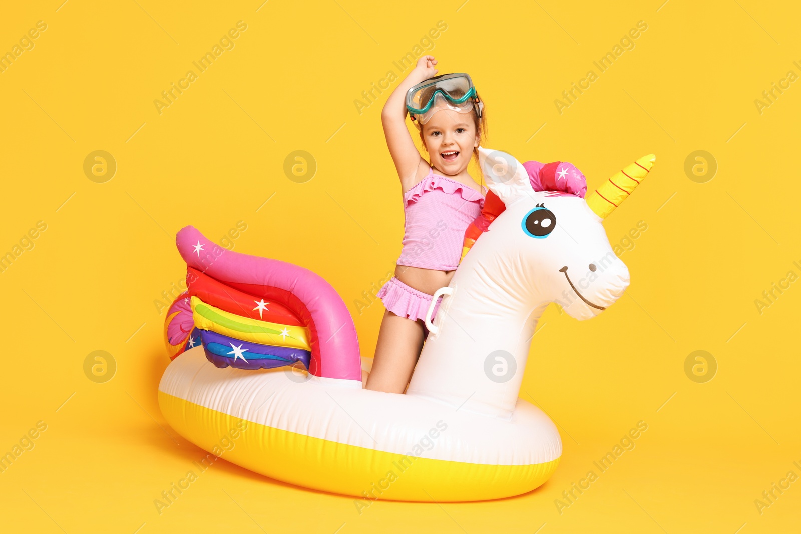 Photo of Cute little girl in swimsuit with unicorn pool float on orange background