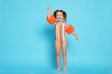 Cute little girl in swimsuit with swim armbands on light blue background