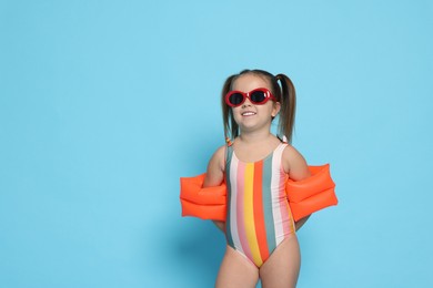 Cute little girl in swimsuit with swim armbands on light blue background. Space for text