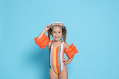 Photo of Cute little girl in swimsuit with swim armbands on light blue background