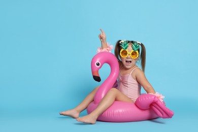 Cute little girl in swimsuit with funny sunglasses and inflatable ring on light blue background. Space for text