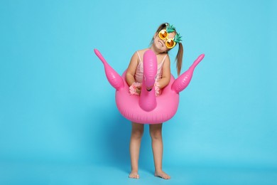 Photo of Cute little girl in swimsuit with funny sunglasses and inflatable ring on light blue background