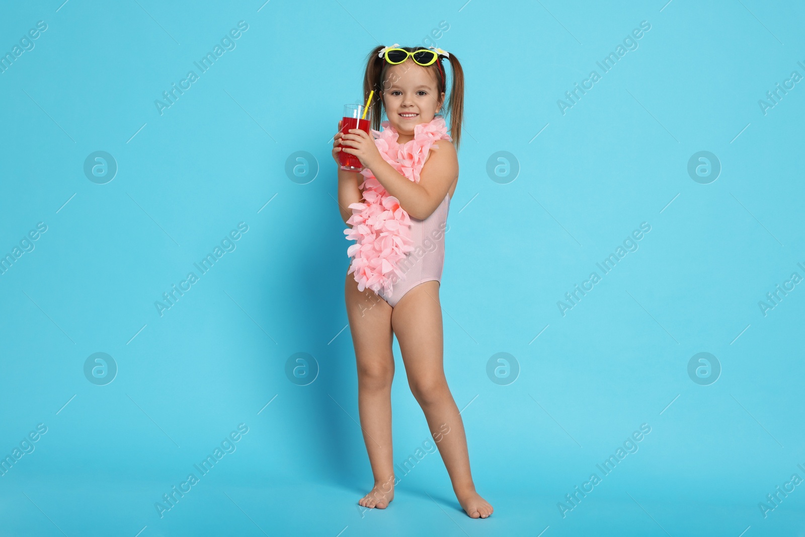 Photo of Cute little girl in swimsuit with drink on light blue background