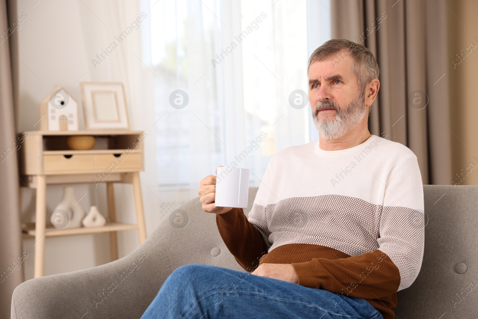 Photo of Mature man with cup of hot drink on sofa at home. Space for text