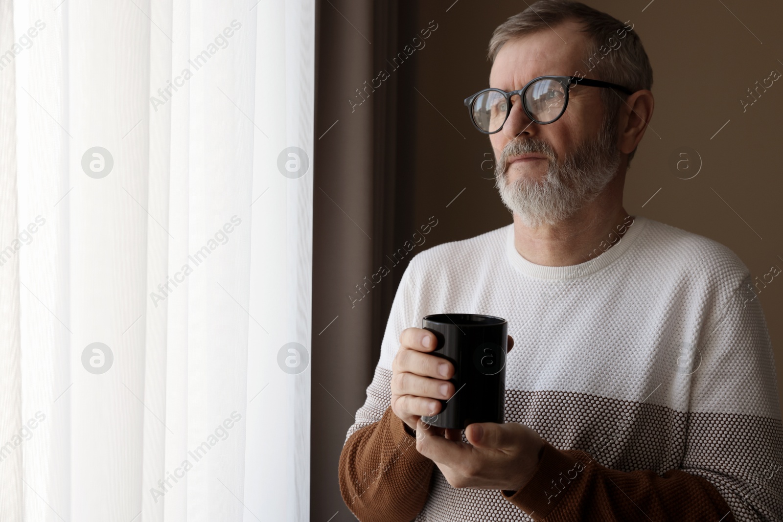 Photo of Mature man with cup of hot drink at home. Space for text