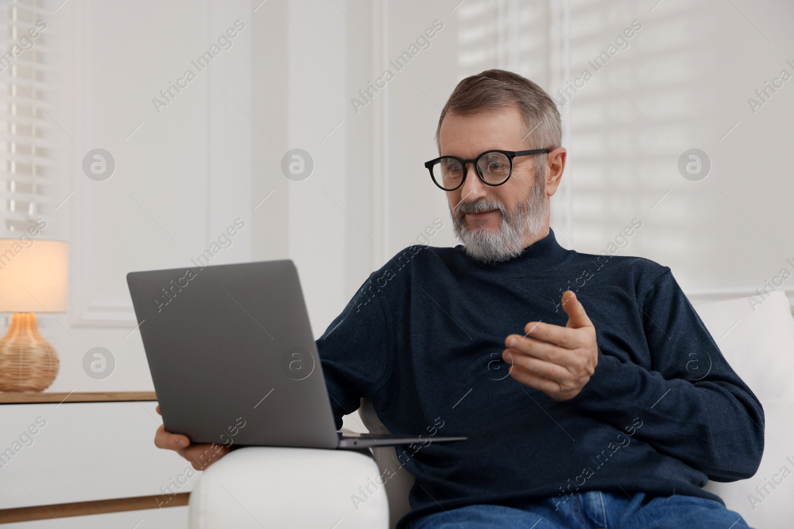 Photo of Mature man having videochat by laptop on sofa at home