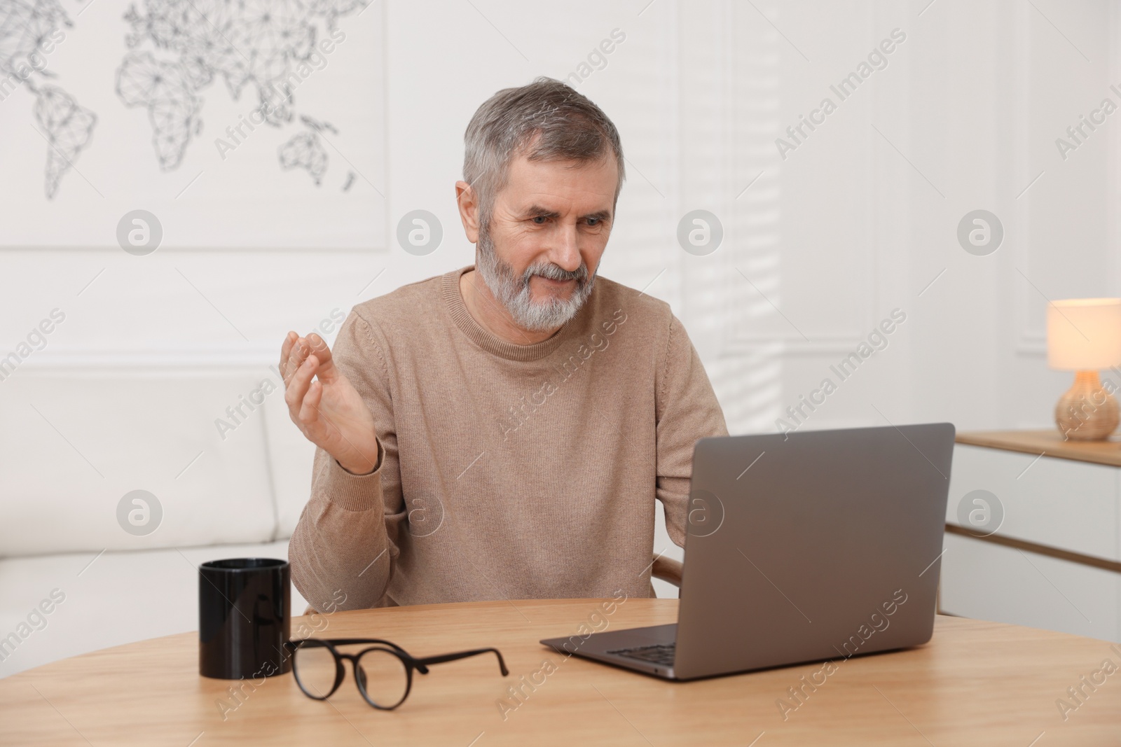 Photo of Mature man having videochat by laptop at table indoors