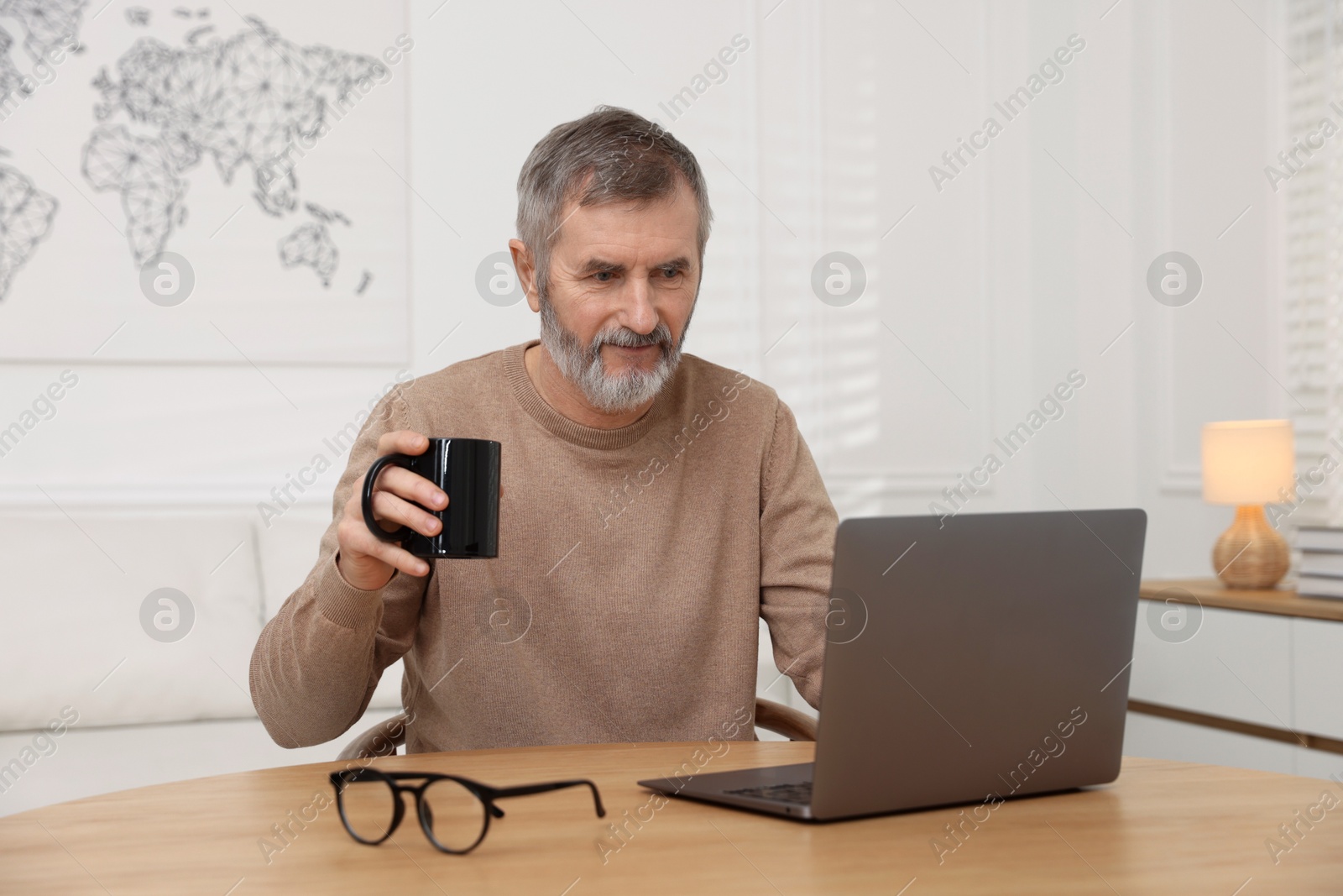 Photo of Mature man having videochat by laptop at table indoors