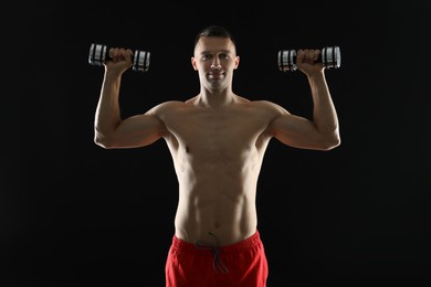 Man exercising with dumbbells on black background