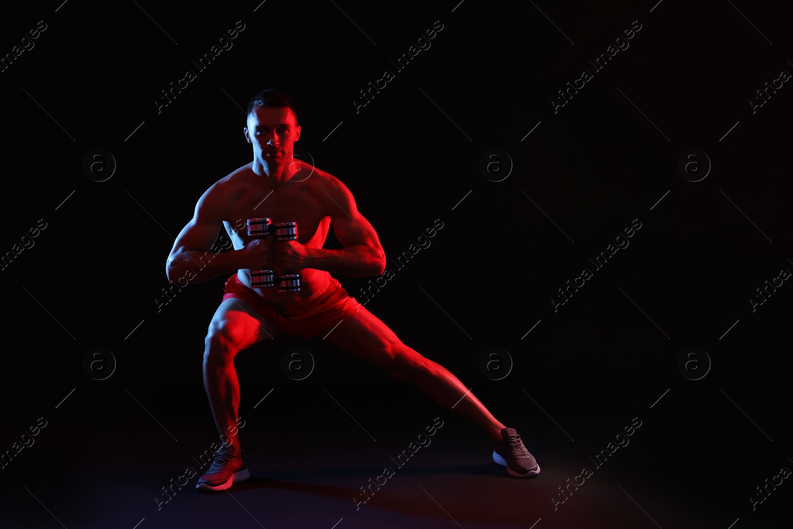 Photo of Man exercising with dumbbells in red light on black background