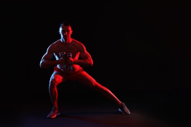 Photo of Man exercising with dumbbells in red light on black background