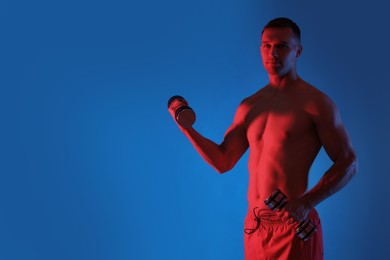 Man exercising with dumbbells in red light on blue background, space for text