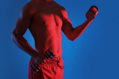 Photo of Man exercising with dumbbells in red light on blue background, closeup