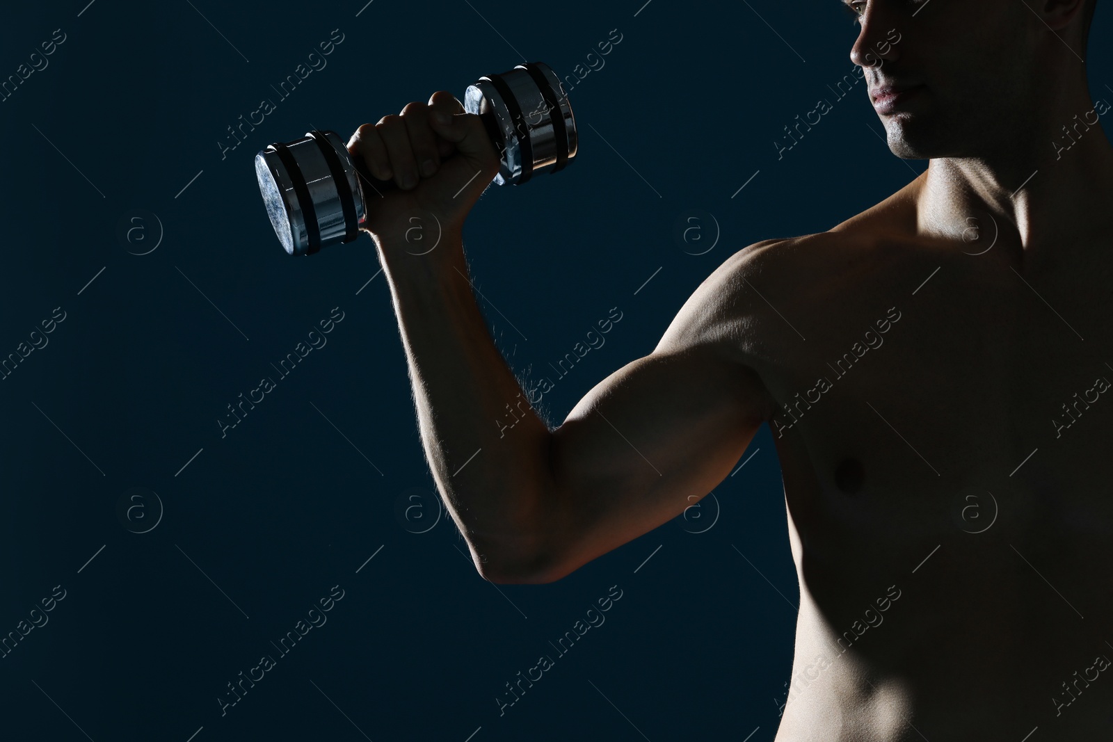 Photo of Man exercising with dumbbell on dark blue background, closeup