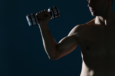 Man exercising with dumbbell on dark blue background, closeup