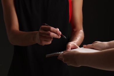 Photo of Sportsman signing autograph in notebook on black background, closeup