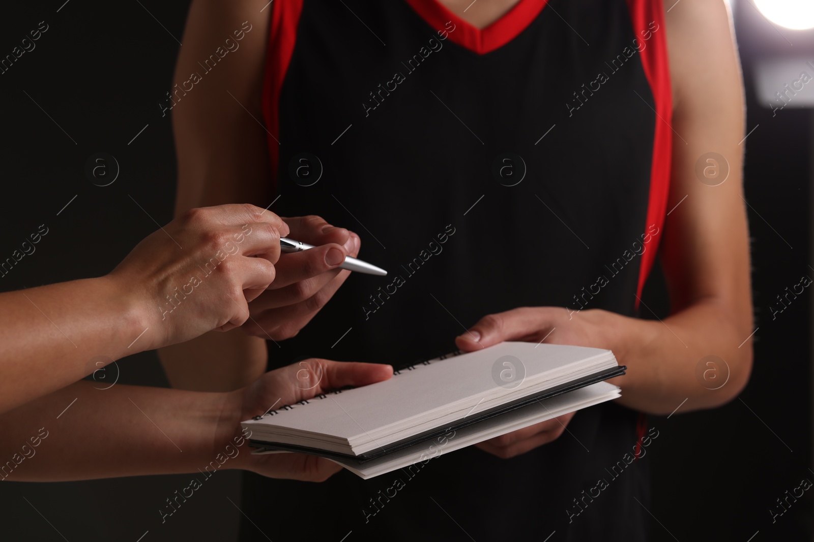 Photo of Sportsman signing autograph in notebook on black background, closeup