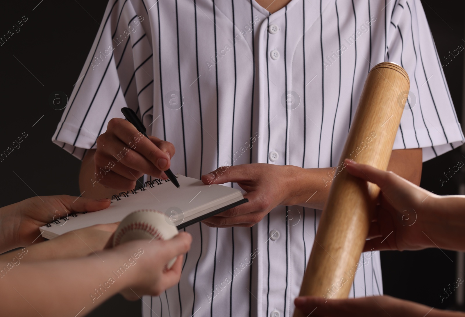 Photo of Baseball player signing autograph in notebook against black background, closeup