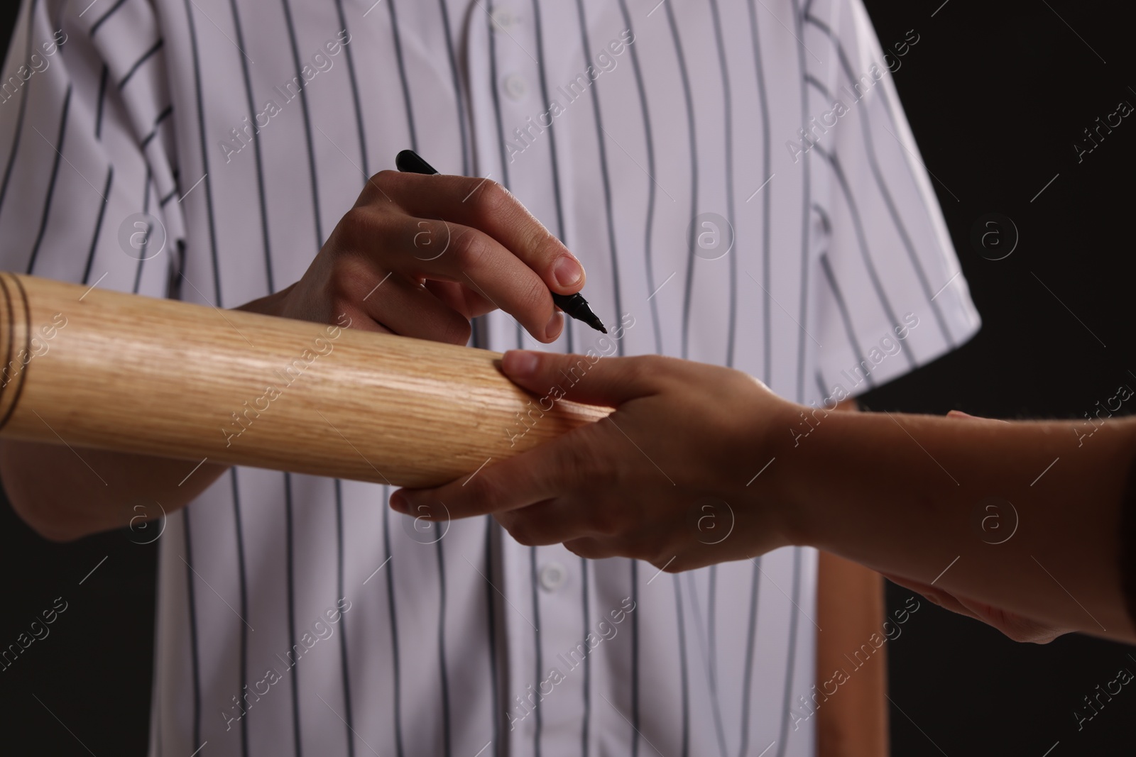 Photo of Baseball player signing autograph on bat against black background, closeup