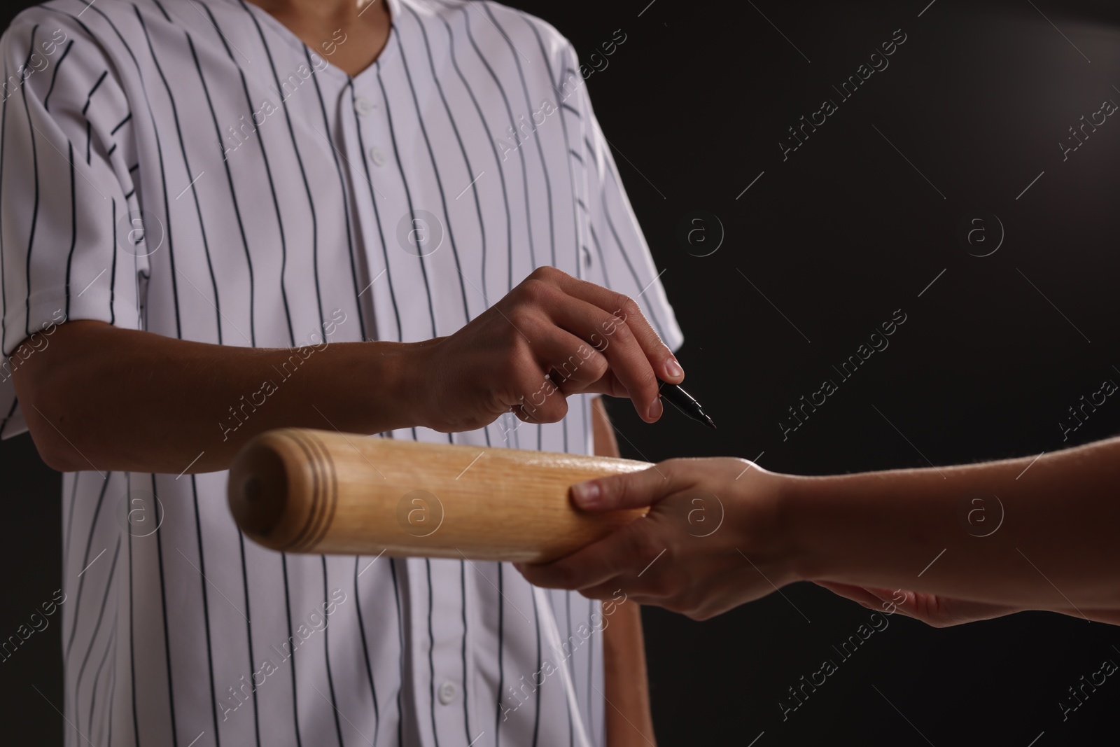 Photo of Baseball player signing autograph on bat against black background, closeup