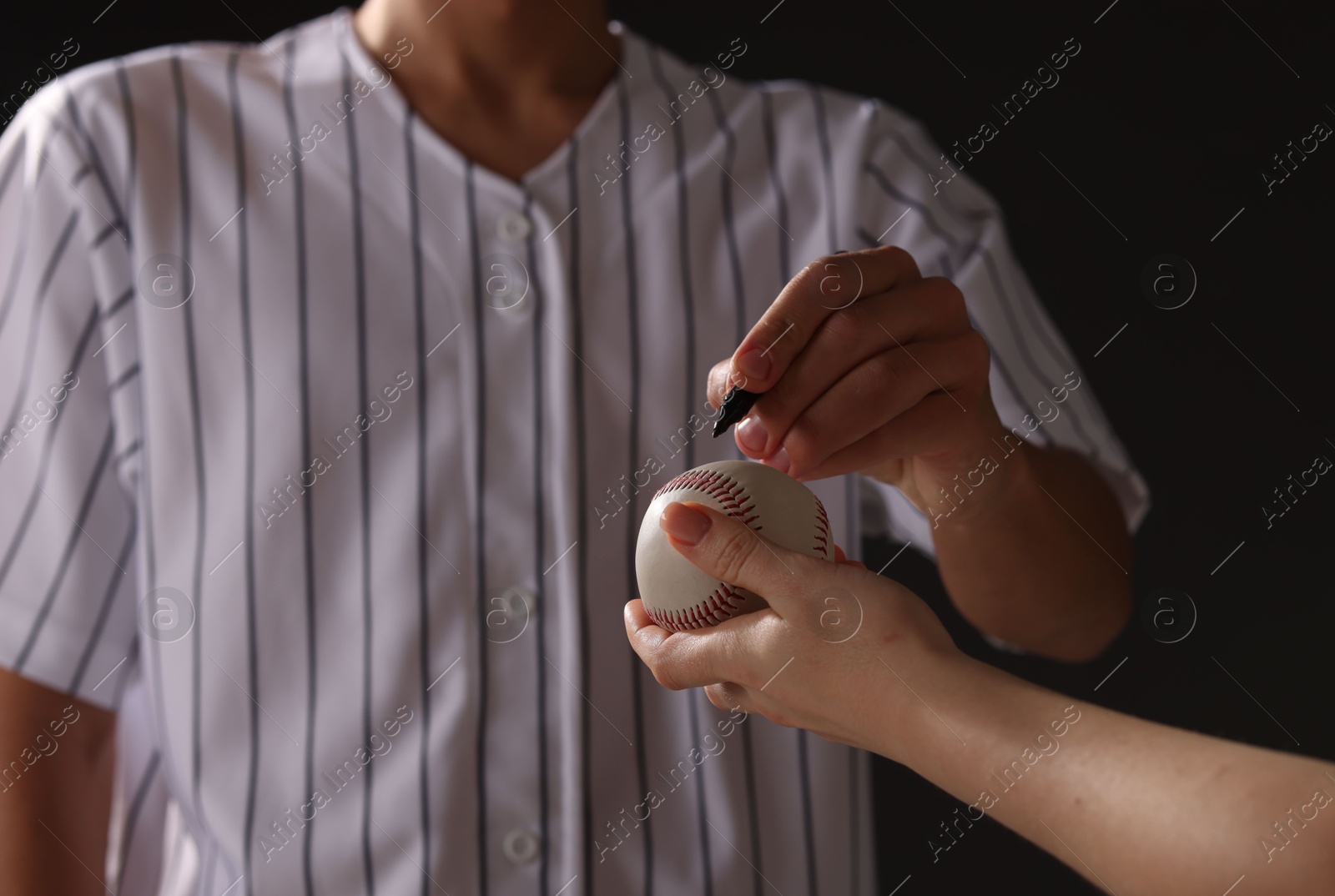 Photo of Baseball player signing autograph on ball against black background, closeup