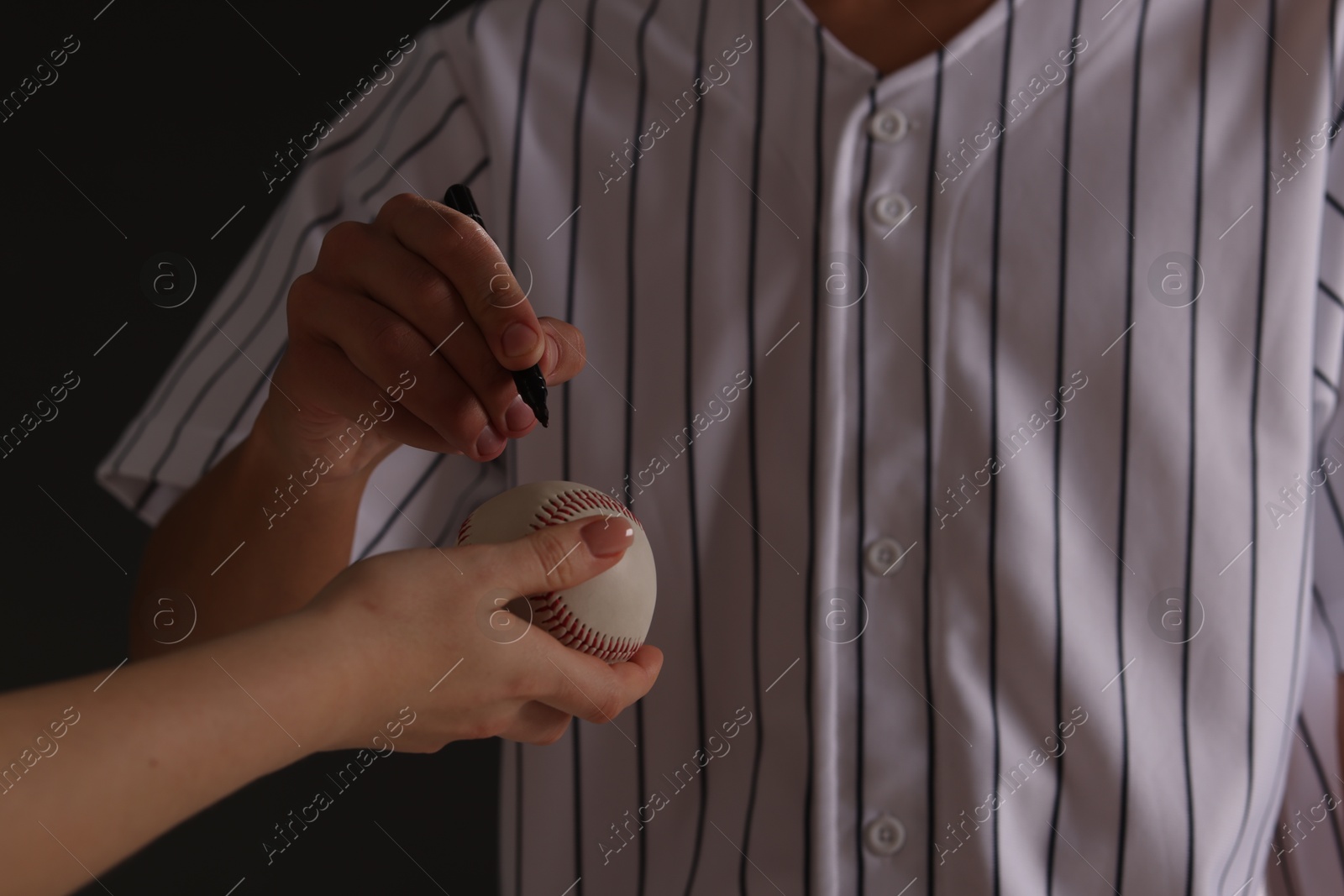 Photo of Baseball player signing autograph on ball against black background, closeup