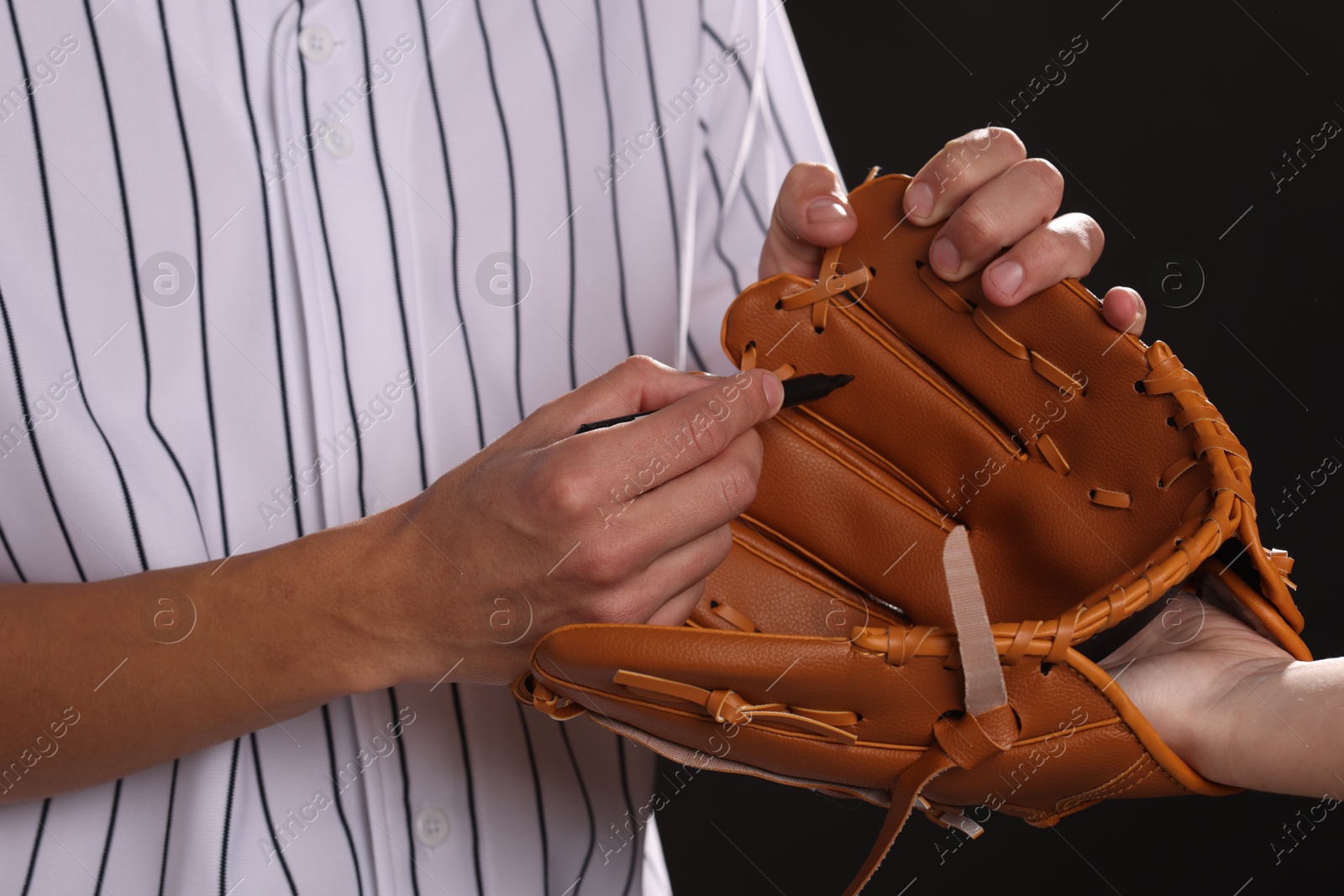 Photo of Baseball player signing autograph on leather glove against black background, closeup