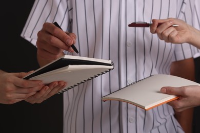 Photo of Baseball player signing autograph in notebook against black background, closeup