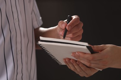 Photo of Baseball player signing autograph in notebook against black background, closeup