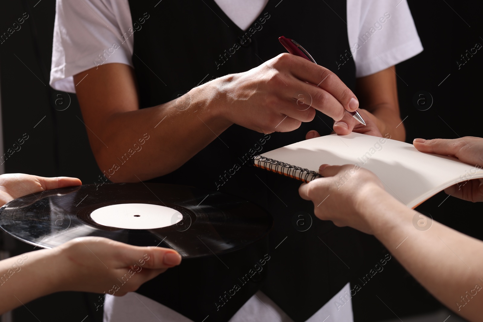 Photo of Singer signing autograph in notebook on black background, closeup