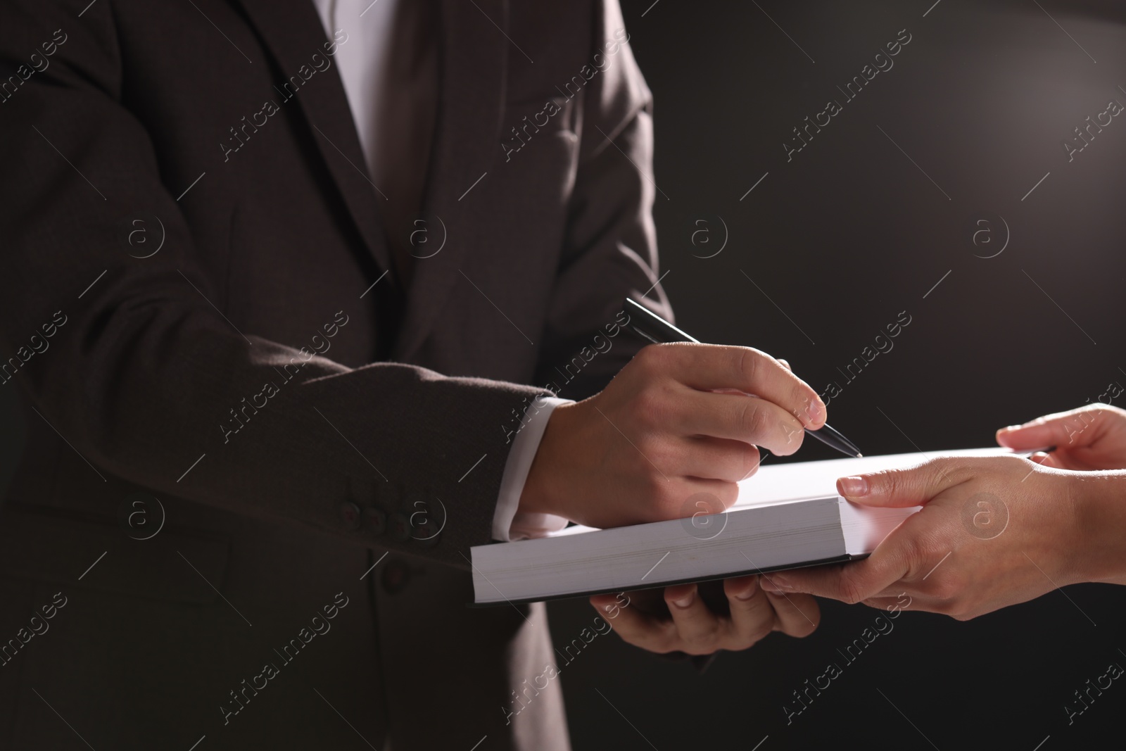 Photo of Writer signing autograph in book on black background, closeup