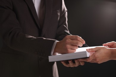 Writer signing autograph in book on black background, closeup