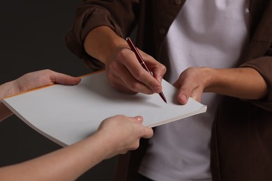 Photo of Man signing autograph in notebook on black background, closeup