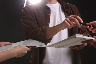 Photo of Man signing autograph in notebook on dark background, closeup