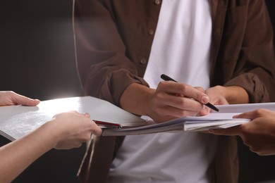 Photo of Man signing autograph in notebook on dark background, closeup