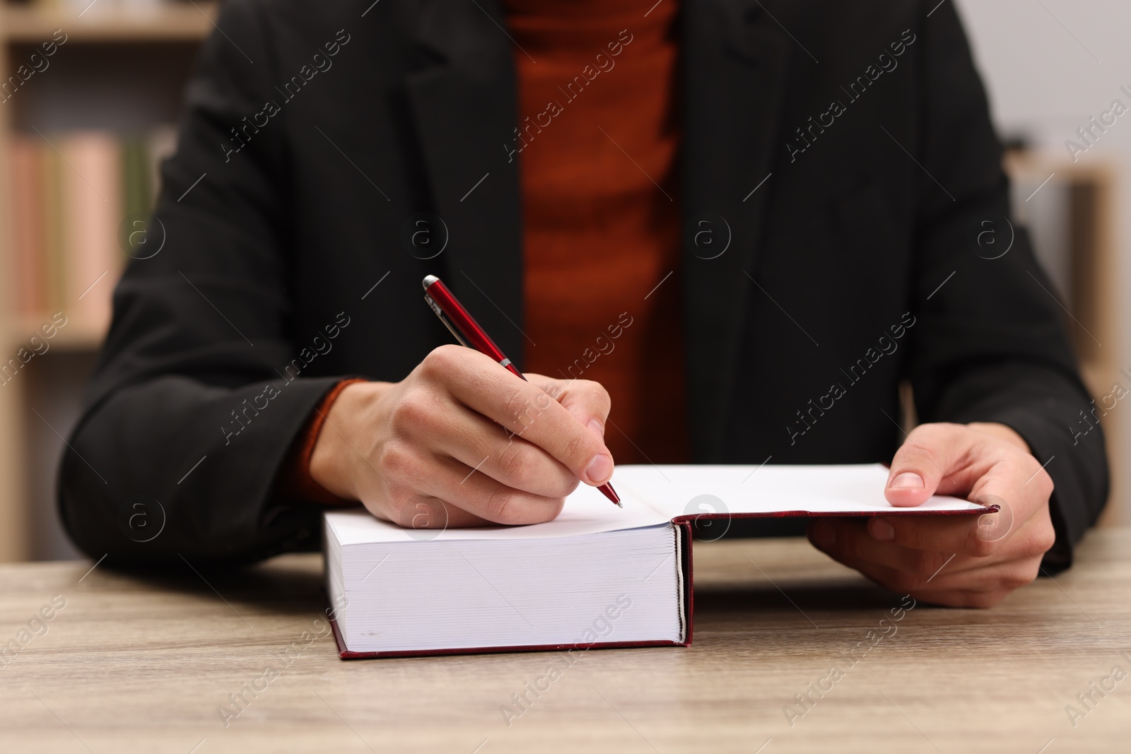 Photo of Writer signing autograph in book at wooden table indoors, closeup