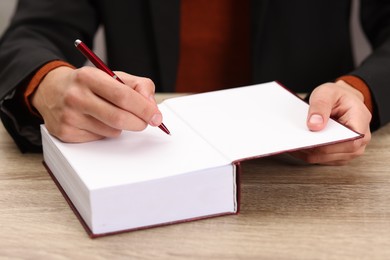 Photo of Writer signing autograph in book at wooden table indoors, closeup