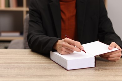 Photo of Writer signing autograph in book at wooden table indoors, closeup