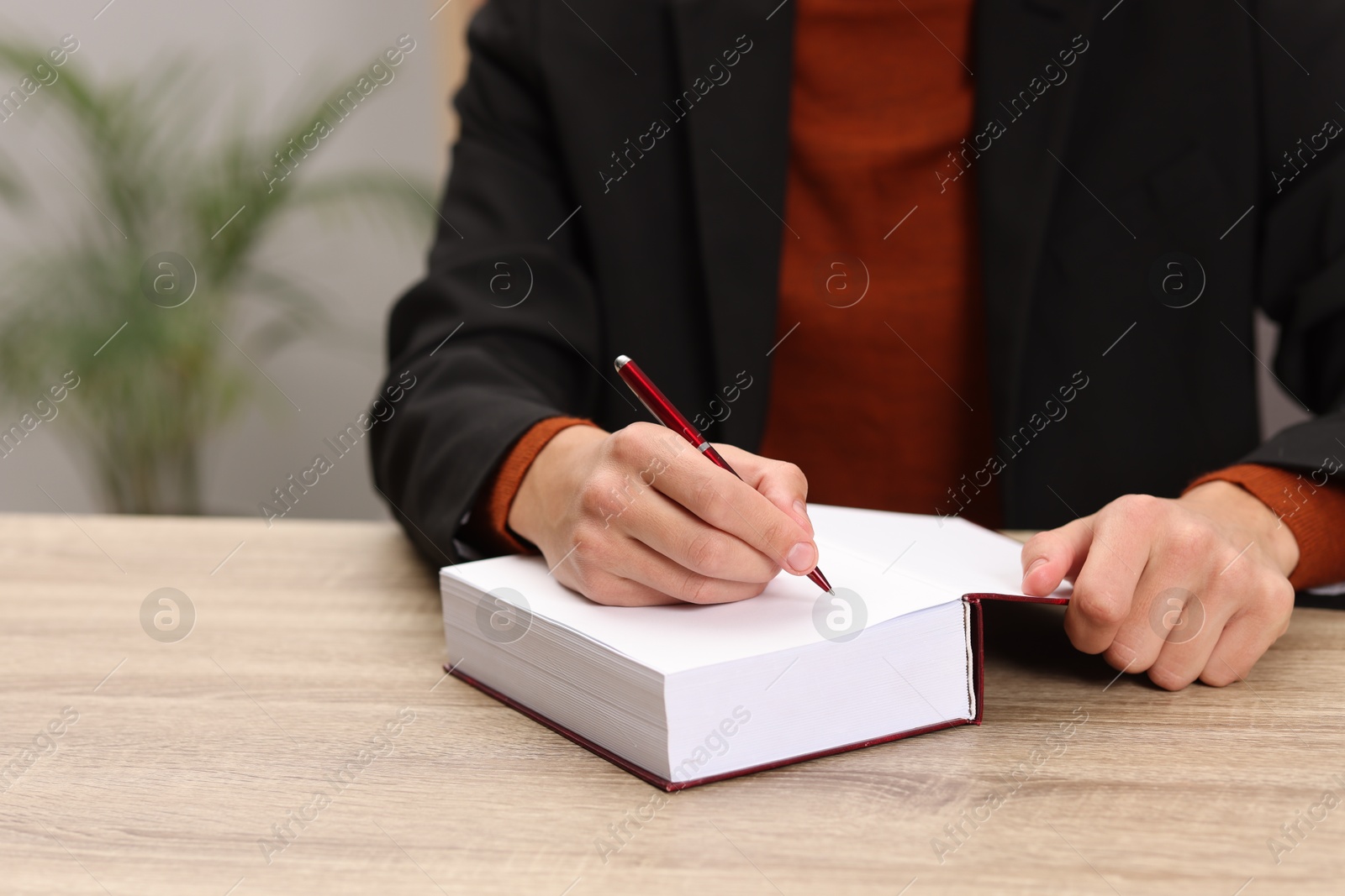 Photo of Writer signing autograph in book at wooden table indoors, closeup