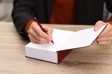 Photo of Writer signing autograph in book at wooden table indoors, closeup