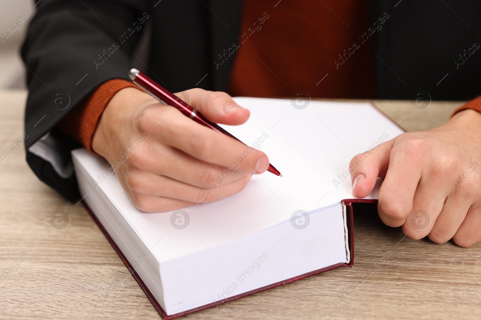 Photo of Writer signing autograph in book at wooden table indoors, closeup