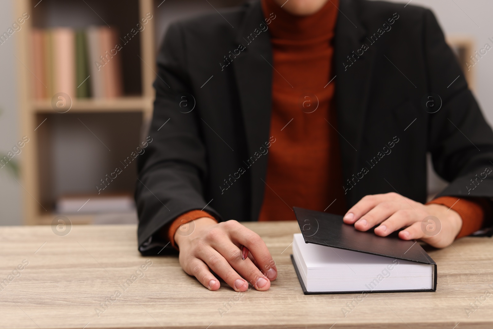 Photo of Signing autograph. Writer with pen and book at wooden table indoors, closeup