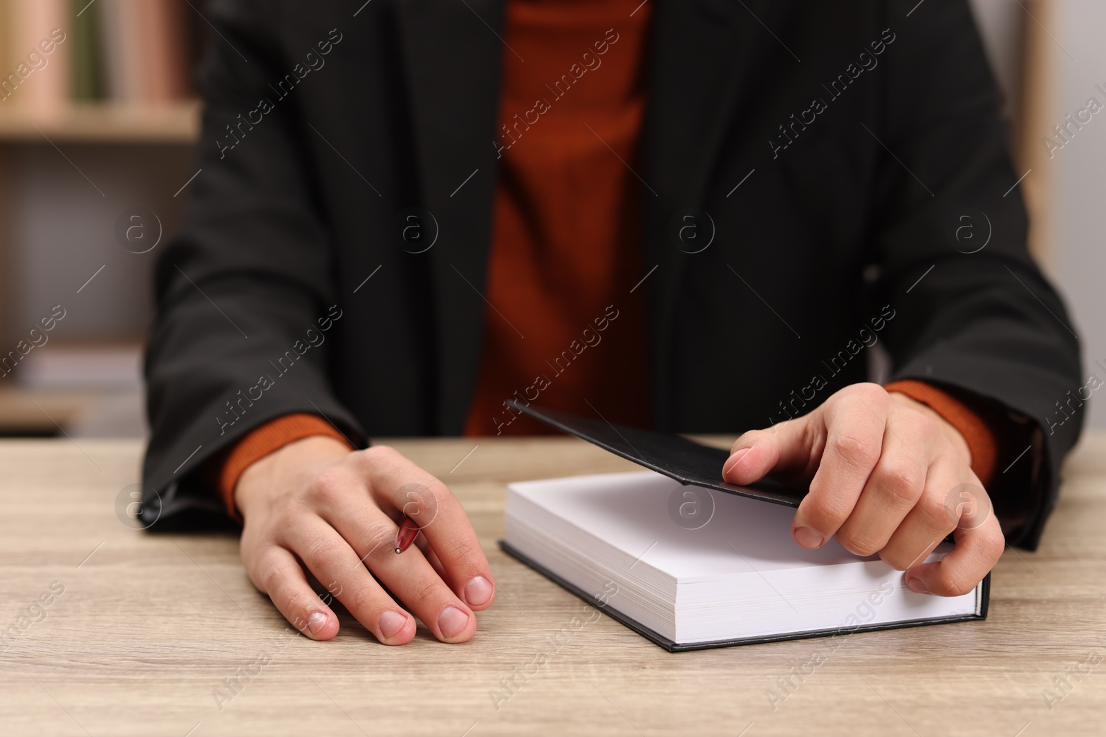 Photo of Signing autograph. Writer with pen and book at wooden table indoors, closeup