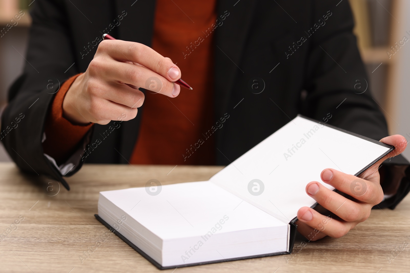 Photo of Writer signing autograph in book at wooden table indoors, closeup