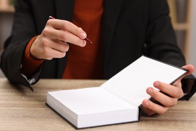 Photo of Writer signing autograph in book at wooden table indoors, closeup