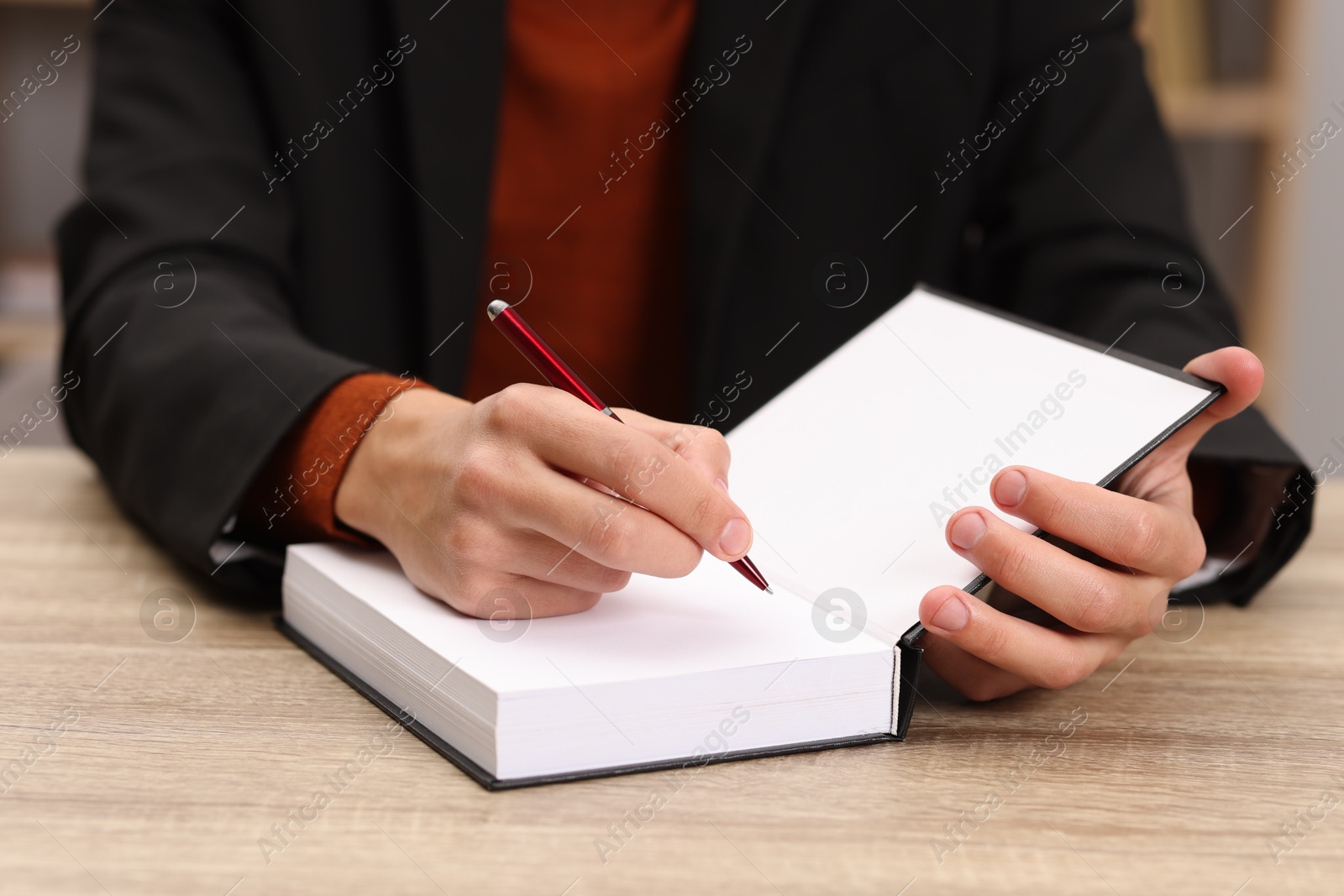 Photo of Writer signing autograph in book at wooden table indoors, closeup