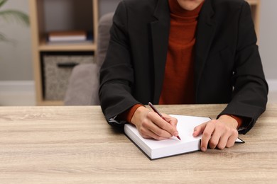 Photo of Writer signing autograph in book at wooden table indoors, closeup