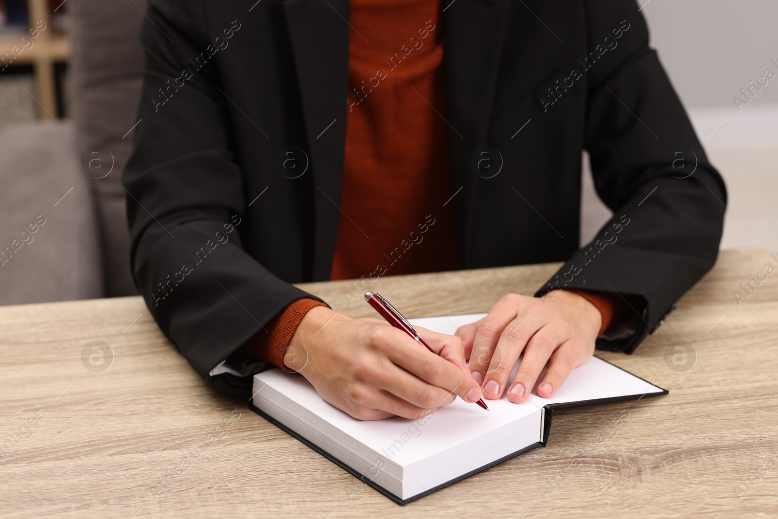 Photo of Writer signing autograph in book at wooden table indoors, closeup