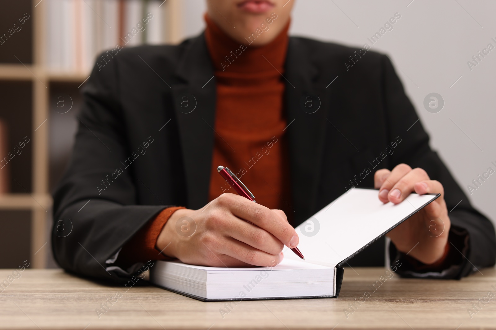 Photo of Writer signing autograph in book at wooden table indoors, closeup