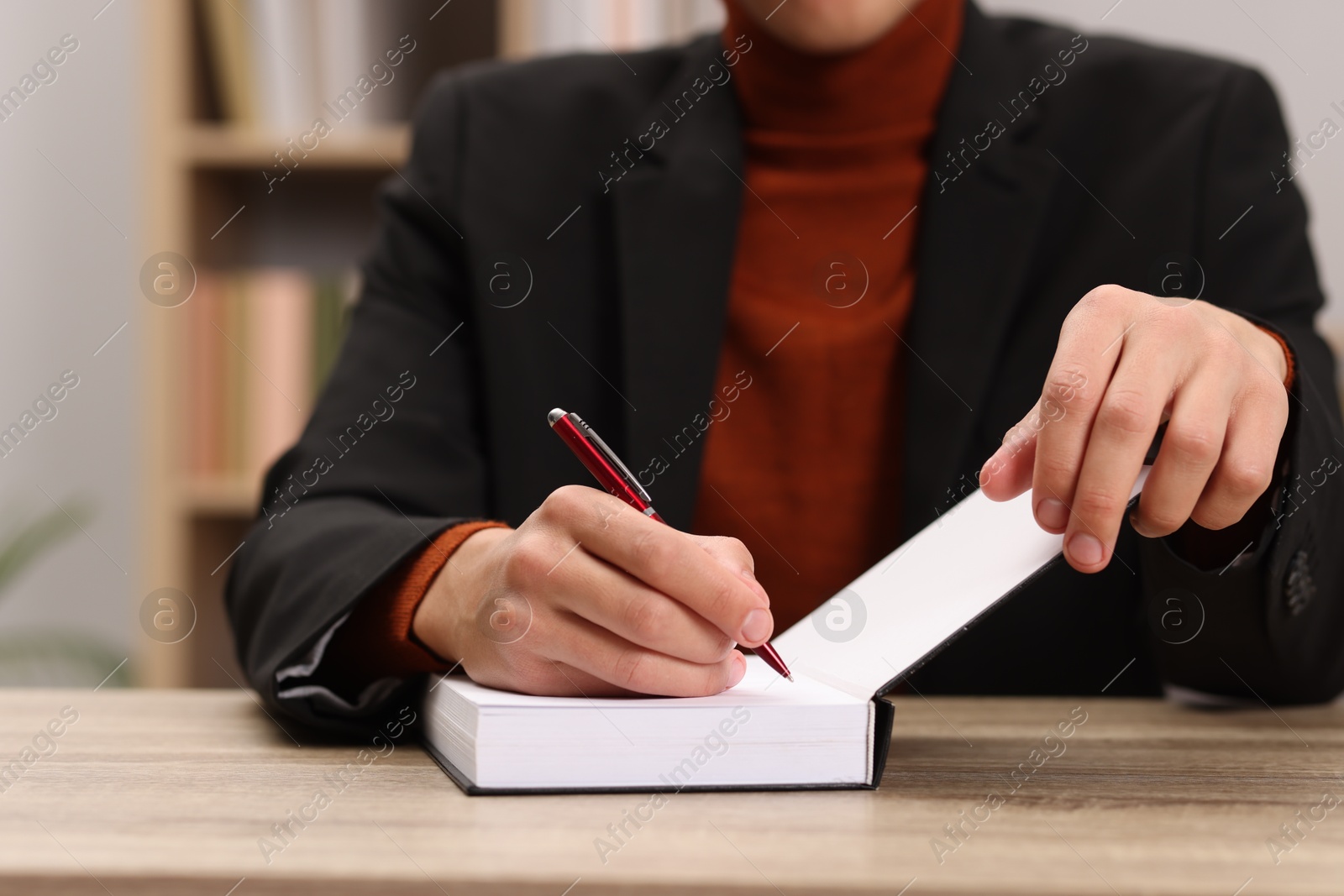 Photo of Writer signing autograph in book at wooden table indoors, closeup